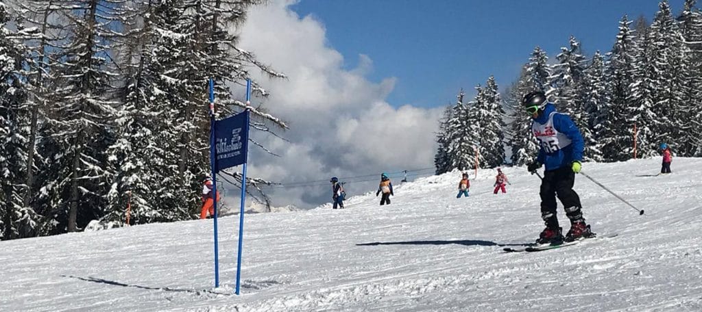 A group of children in colorful ski gear enjoying a winter day on a snowy slope in Austria, surrounded by pine trees and mountains.